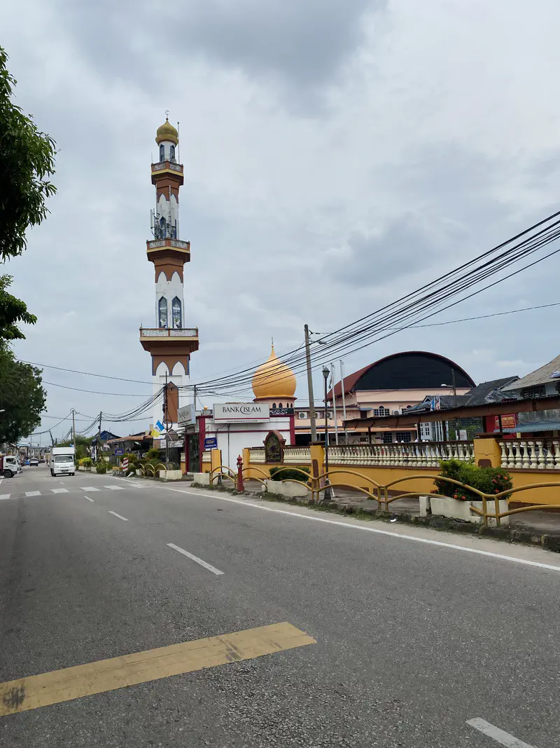 Street view with a tall mosque minaret and golden dome in the background, next to a Bank Islam building.