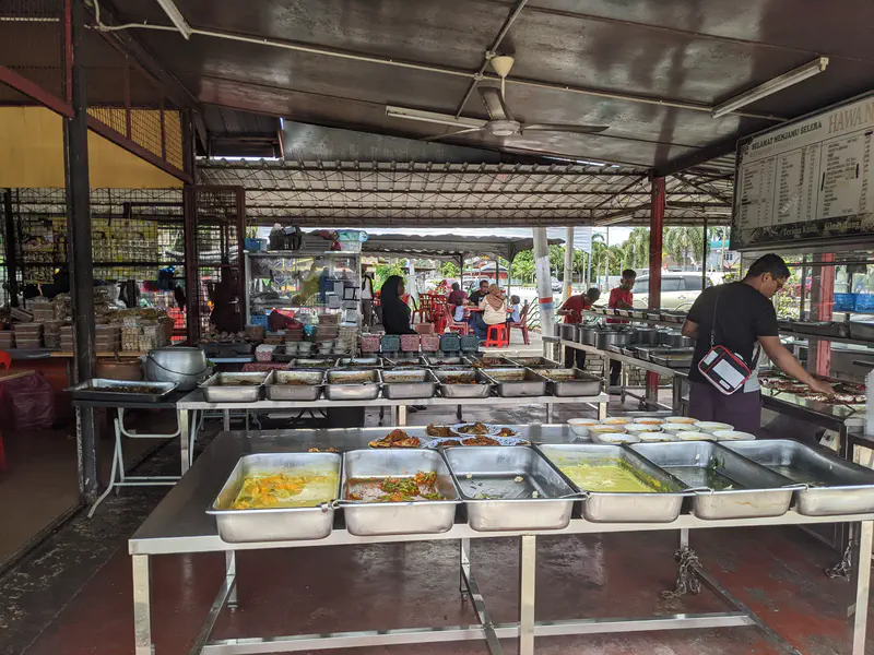 Buffet-style setup with trays of various Malaysian dishes in an open-air eatery.