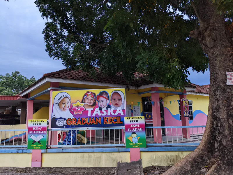 Colorful kindergarten building named 'Taska Graduan Kecil' with large posters of children displayed at the entrance.