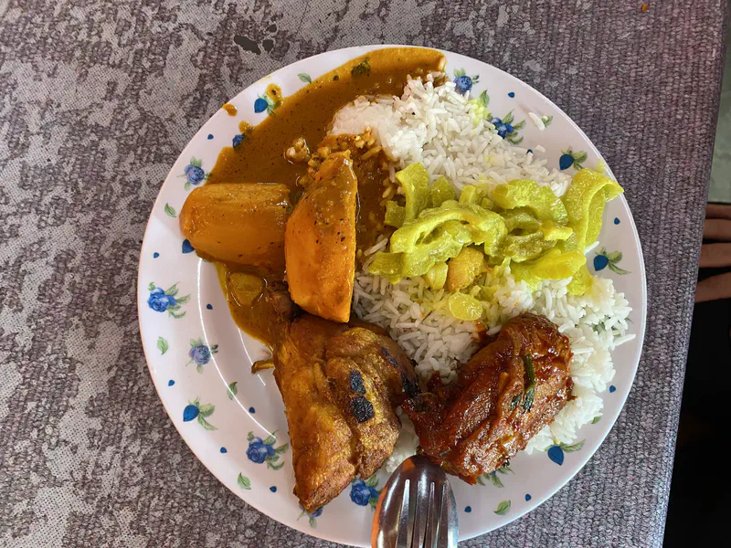 Plate of nasi lemak with white rice, curry sauce, fried chicken, sambal chicken, and bitter gourd stir-fry.