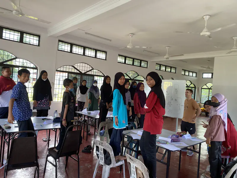 Group of children standing in a classroom with a teacher near a whiteboard.