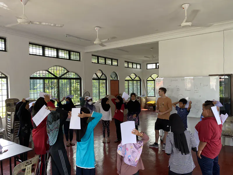 Children holding papers on their heads while standing in a circle during a classroom activity.