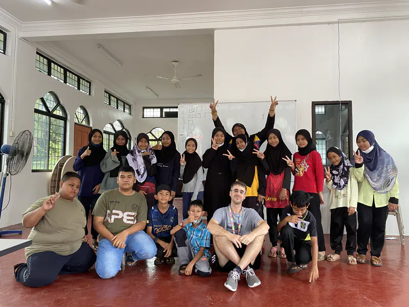 Group of children and an adult posing together in a classroom with a whiteboard behind them.
