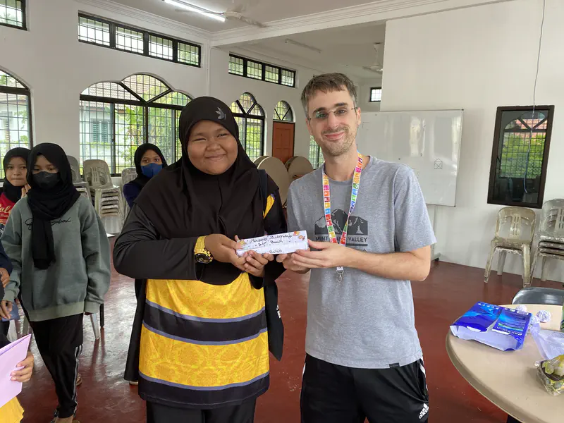 Man and girl smiling while holding a note together in a classroom setting.