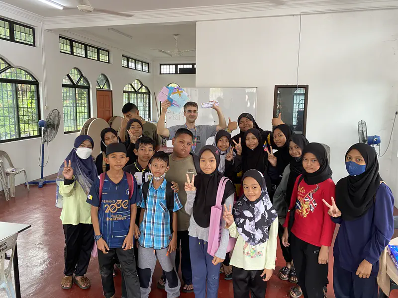 Group of children posing with their teacher in a classroom, holding up cards and smiling.