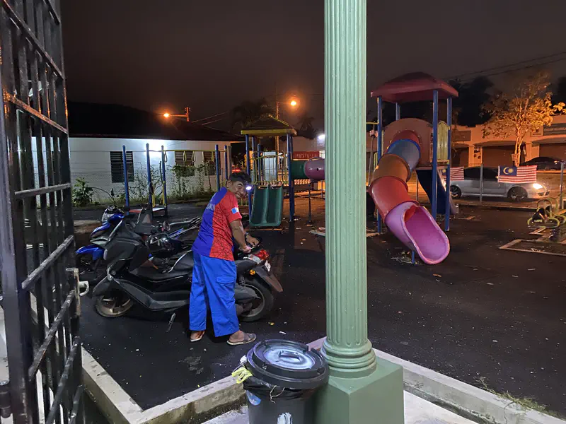 Man standing beside a parked motorcycle at night near a playground with slides.