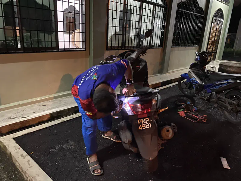 Man repairing the back of a motorcycle at night beside a building.
