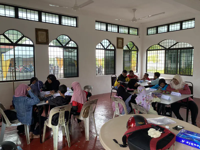 Children seated in groups around tables working on activities inside a bright classroom.