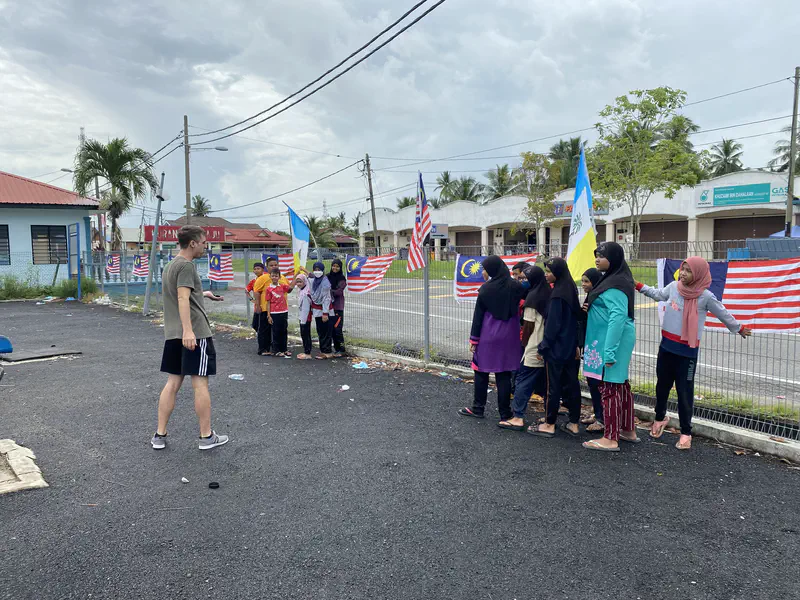 Children standing in teams holding flags while a teacher gives instructions outdoors.