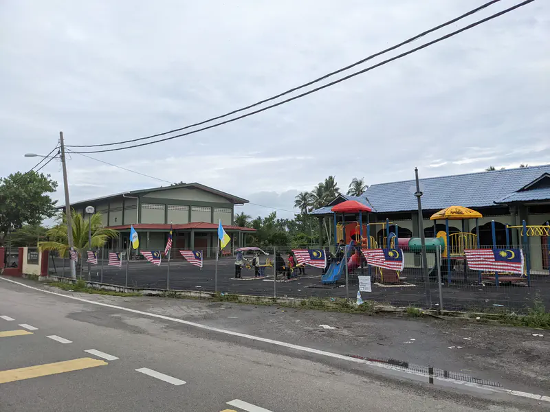 Community building and playground decorated with Malaysian and state flags along the fence.