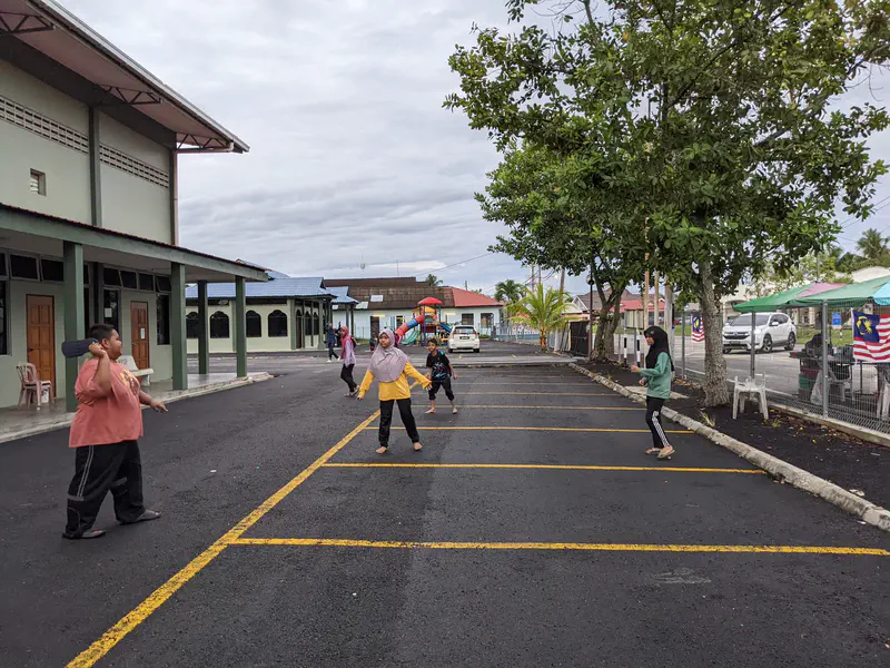 Children playing outdoors in a parking lot, with one boy holding a sandal ready to throw.