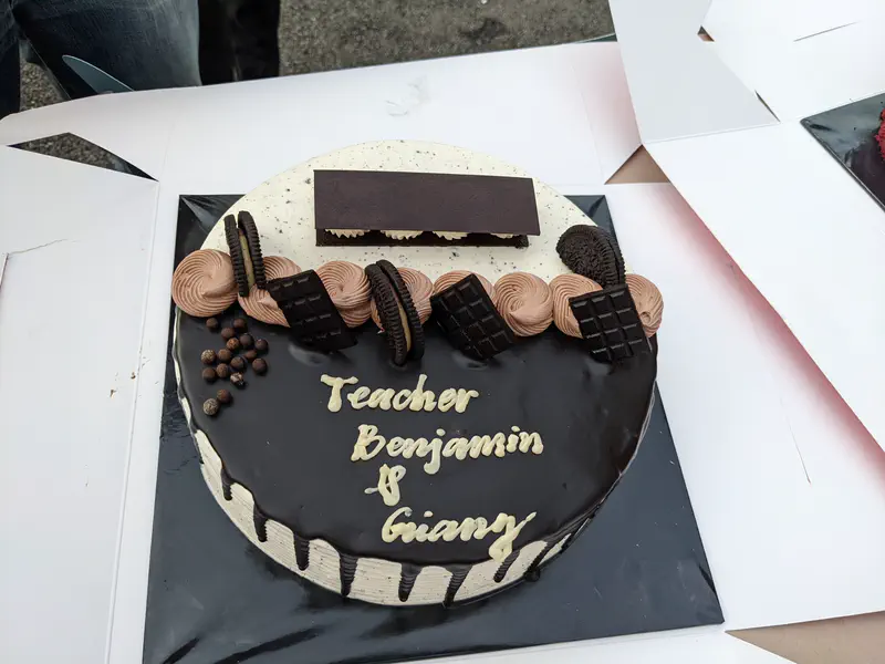 Chocolate cake with cookies and decorations, inscribed with 'Teacher Benjamin & Giang'.