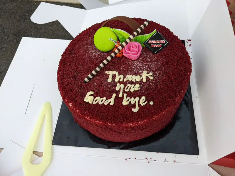 Red velvet cake decorated with chocolate and a flower, inscribed with 'Thank you goodbye'.