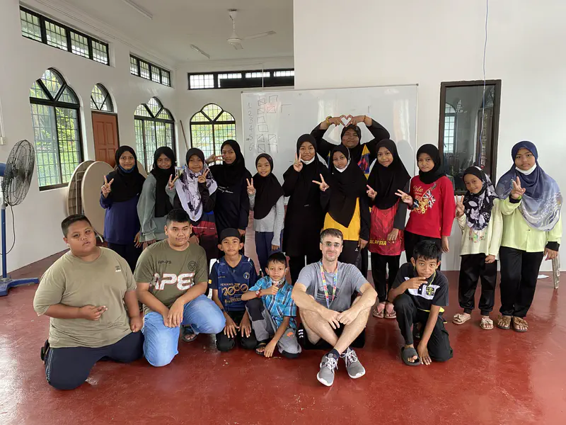 Group of children and adults posing together in a classroom with a whiteboard behind them.