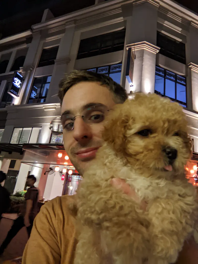 Person holding a fluffy brown puppy at night in front of a lit building.