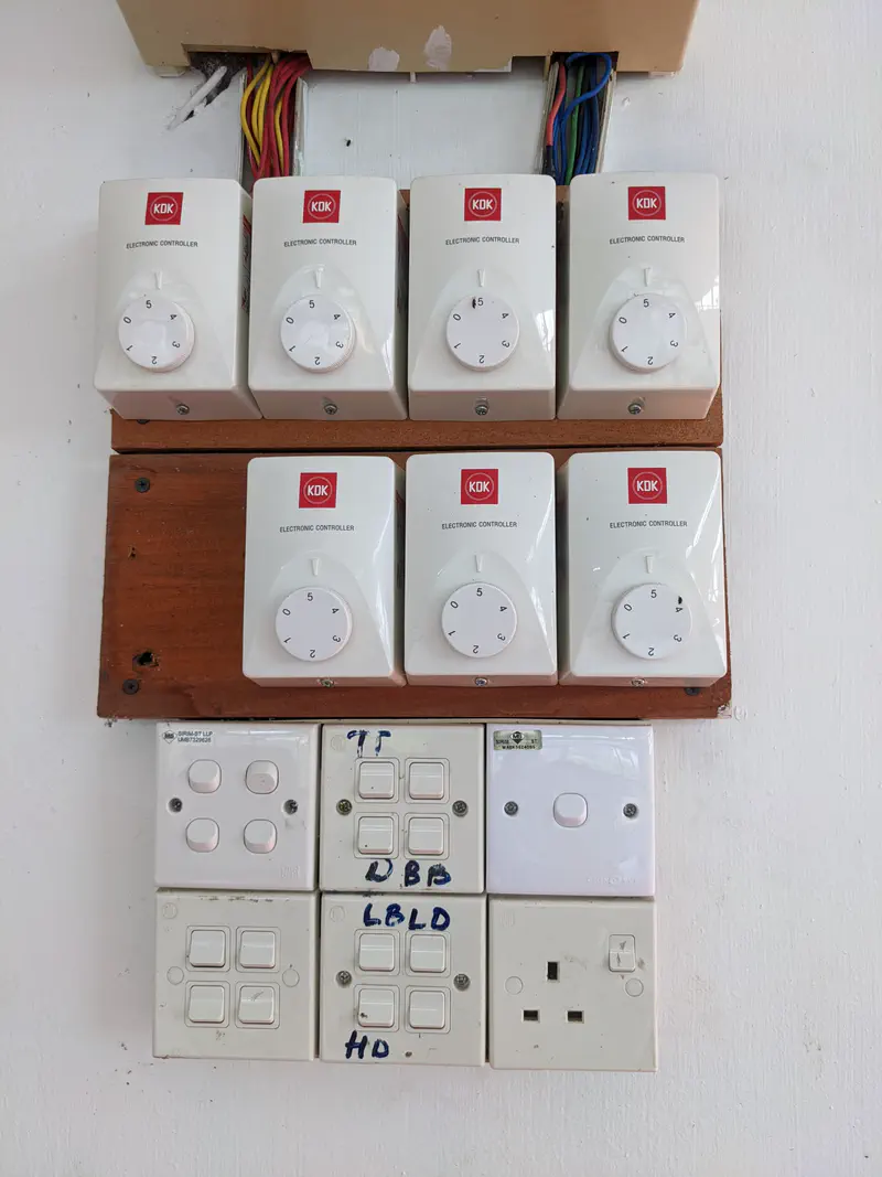 Wall panel with multiple KDK electronic controllers, switches, and power outlets.