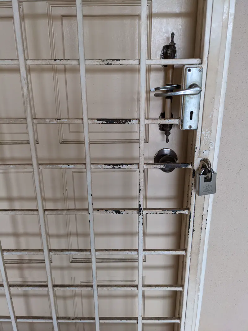 Metal security gate with padlock in front of a closed wooden door.