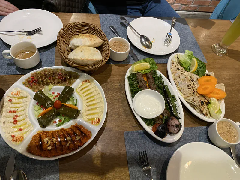 Table with Middle Eastern dishes including hummus, stuffed grape leaves, kebabs, flatbreads, and tea.