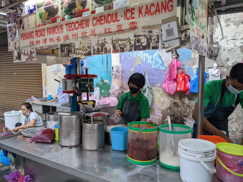 Street food stall with workers preparing bowls of chendul dessert.
