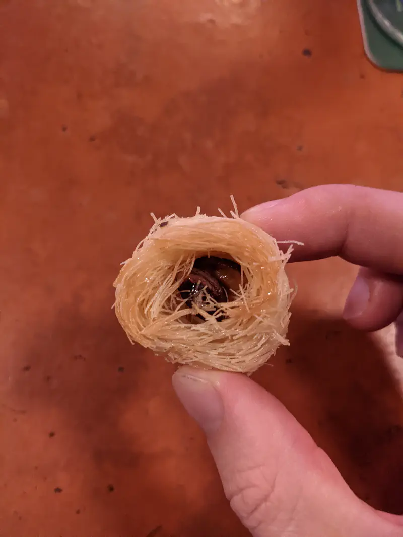 Hand holding a piece of Middle Eastern dessert made with shredded pastry and nuts.