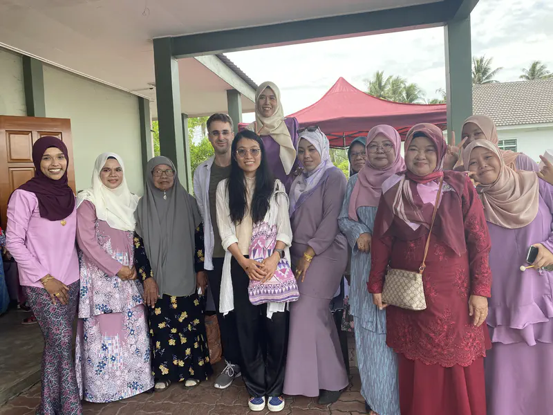 Group photo of guests, including women in traditional attire, smiling together at a Malay wedding event.