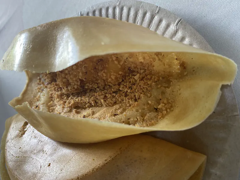 Street food stall vendors preparing apam balik pancakes on a griddle under a blue canopy.