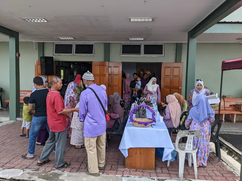 Guests gathered outside a hall entrance during a Malay wedding celebration, with women in traditional attire seated at a reception table.