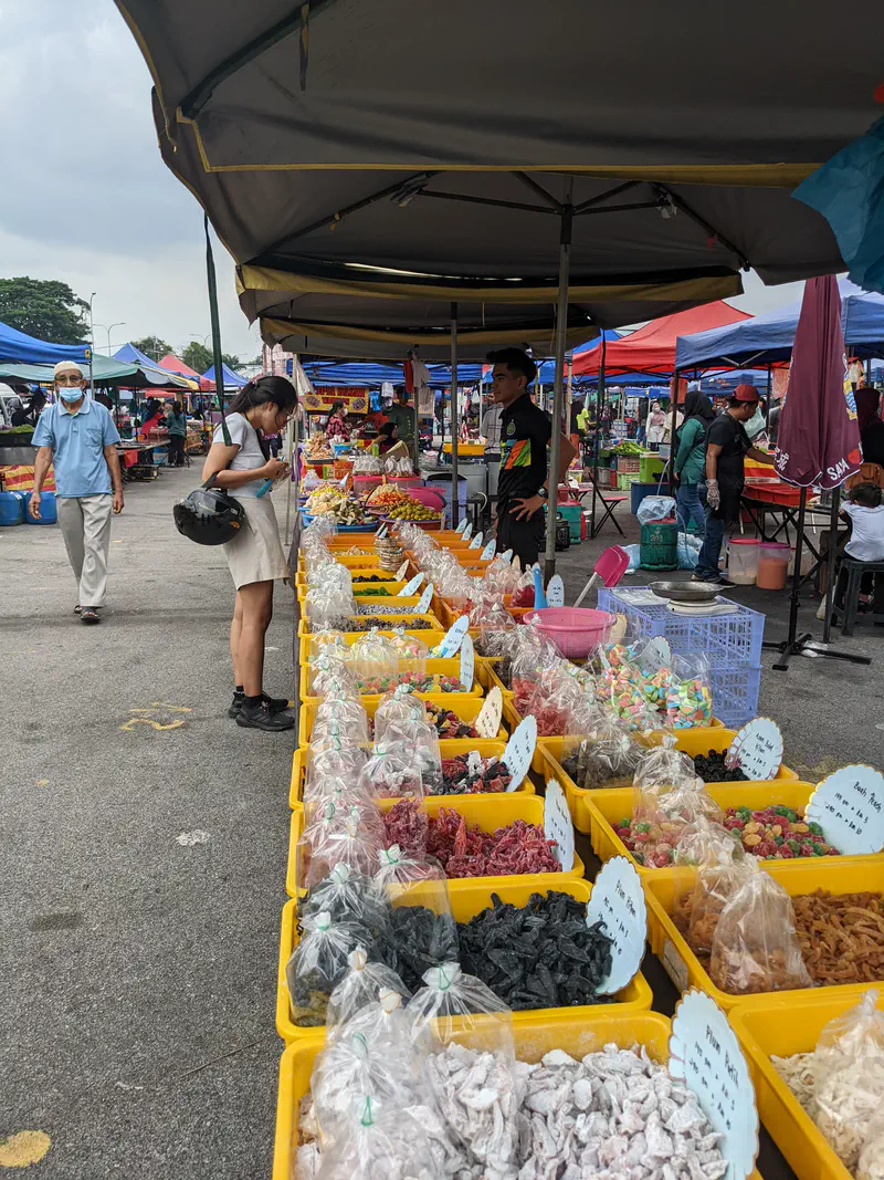 Market stall with rows of colorful dried fruits and snacks in plastic bags displayed in yellow bins.