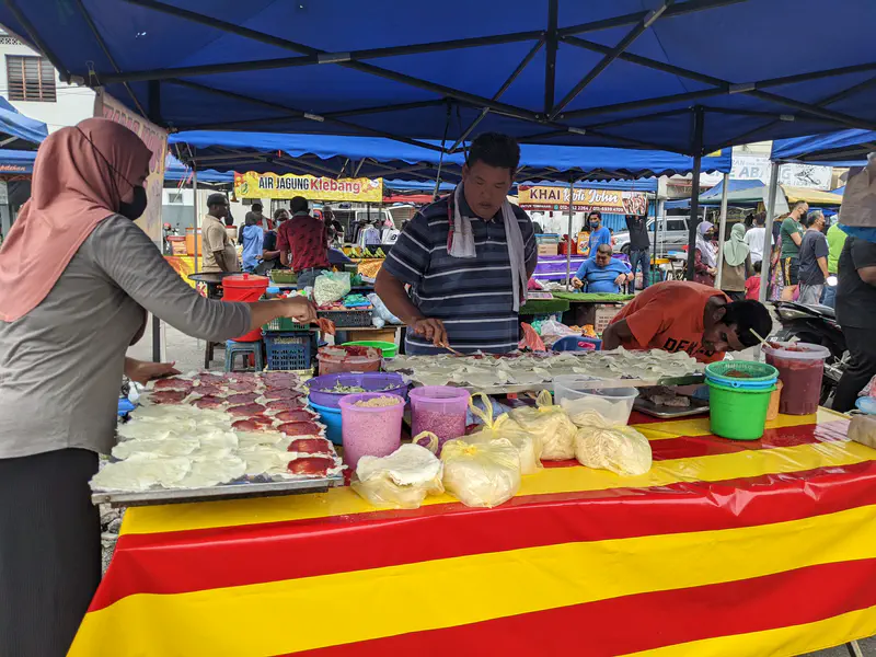 Vendors preparing fresh popia basah with ingredients spread on wrappers at a market stall.