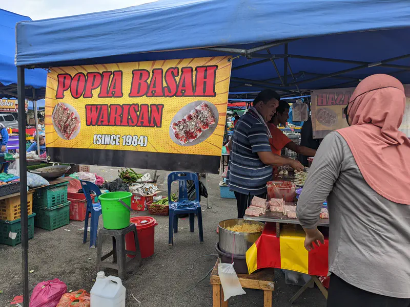 Popia Basah Warisan stall with a large yellow sign advertising the traditional Malaysian spring rolls since 1984.