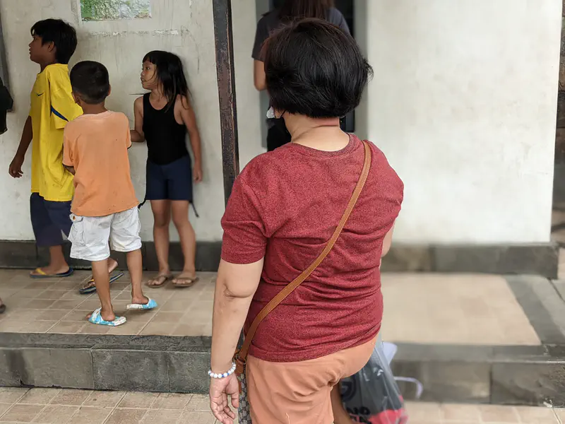 Woman in a red shirt standing near children in casual clothes by a building entrance.