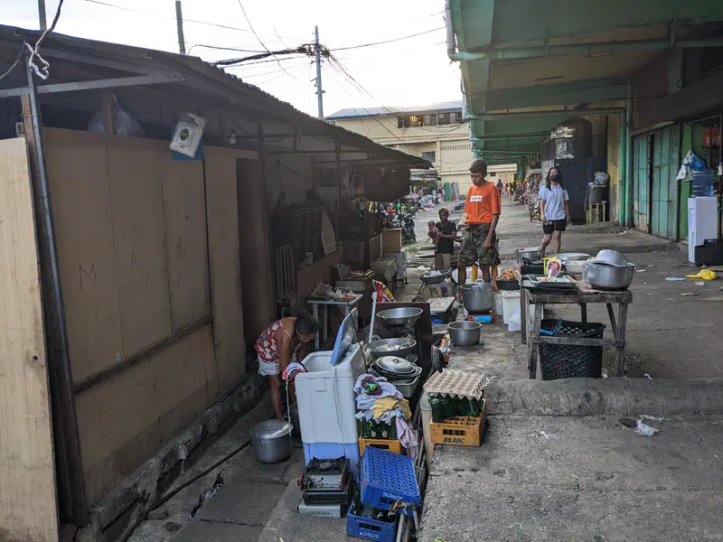 Street scene with people cooking and washing dishes outdoors beside makeshift stalls.