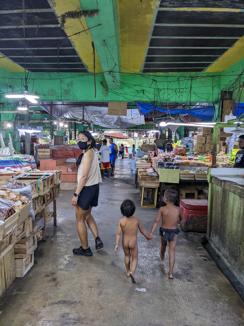 Market aisle with a woman in a mask walking beside two small children holding hands.