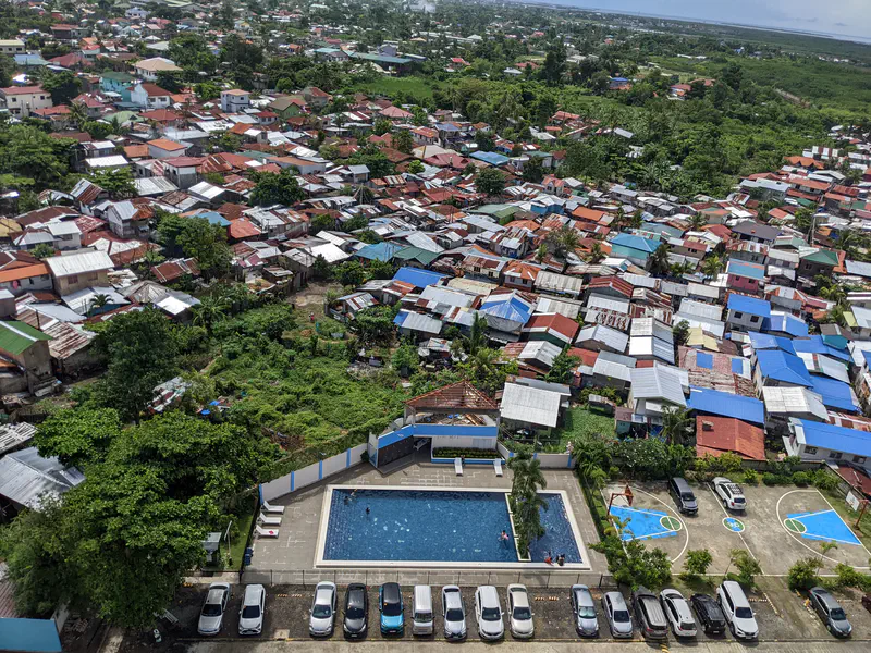 Aerial view of a crowded neighborhood with colorful rooftops and a nearby pool and basketball court.