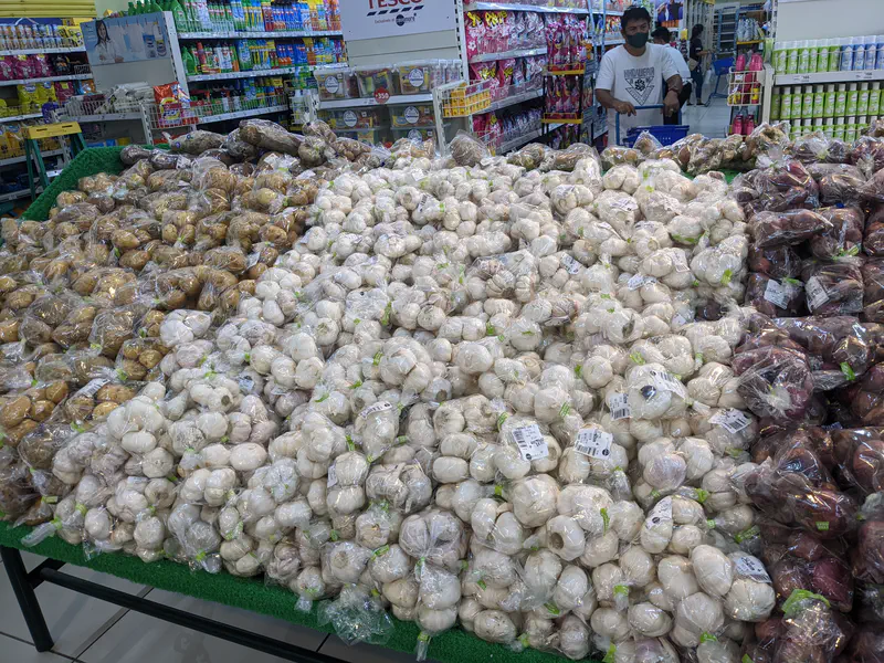 Piles of bagged garlic, potatoes, and other vegetables displayed in a supermarket.