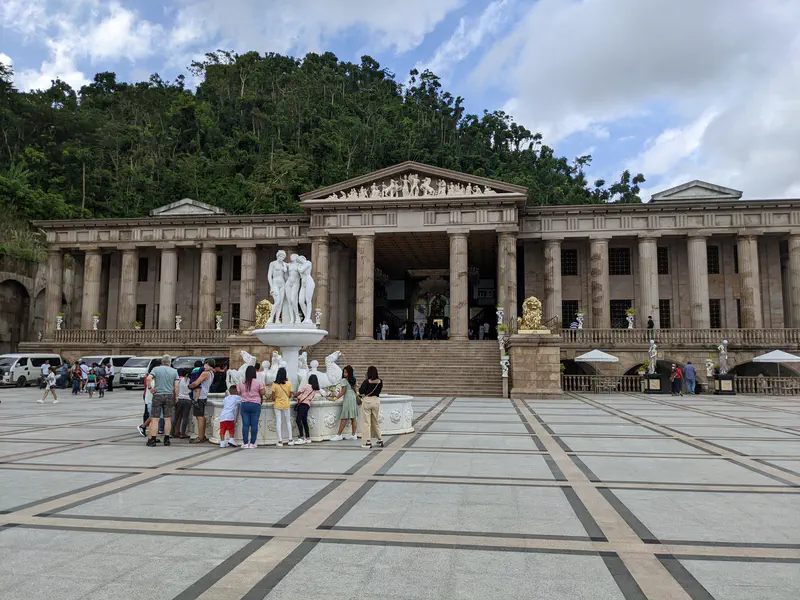 Neoclassical-style building with tall columns, a statue fountain, and visitors in the courtyard.