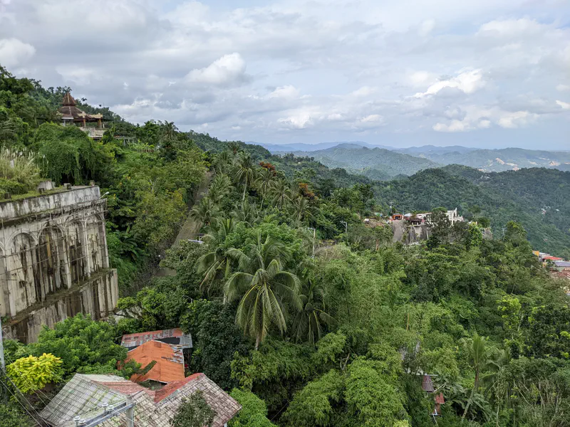 Scenic view of lush green mountains and scattered houses under a partly cloudy sky.