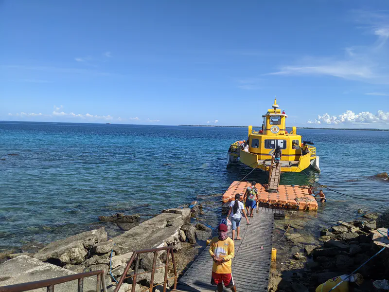Bright yellow boat docked at a floating pier with people boarding by the sea.