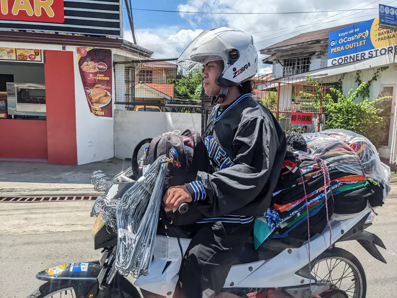 Man riding a motorcycle loaded with clothes and metal hangers for sale.