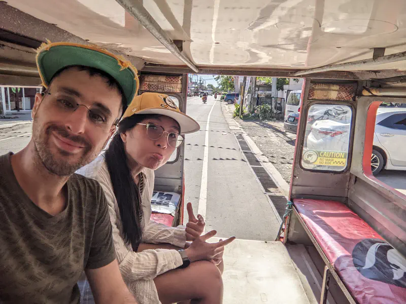 Two people sitting inside a jeepney smiling and making playful gestures during a ride.