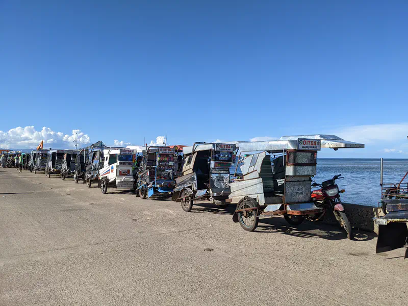 Row of tricycles parked along a coastal road with the ocean in the background.