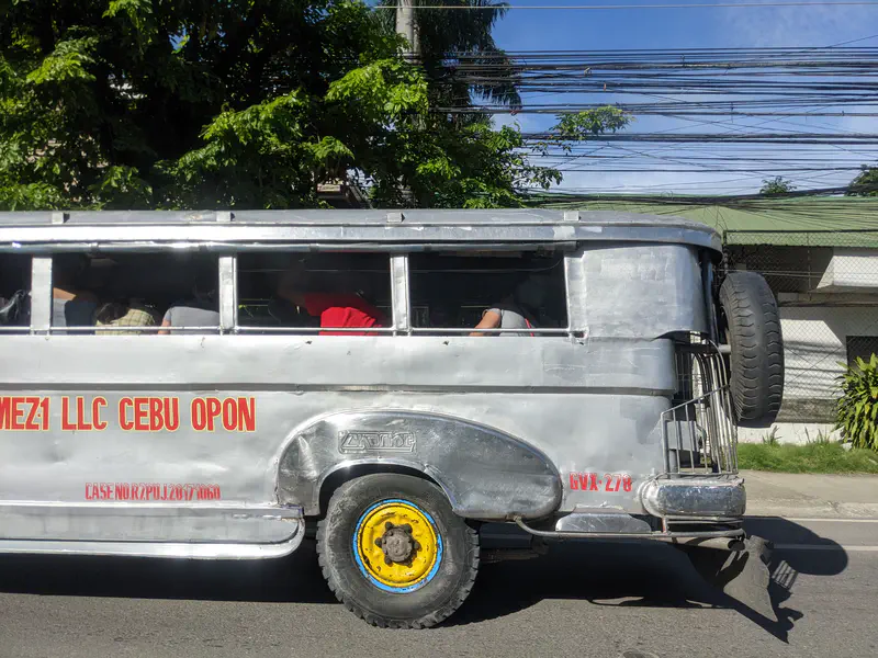 Side view of a silver jeepney with yellow wheels, carrying passengers along a street in Cebu.