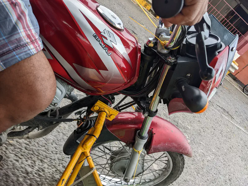 Close-up view of a red Bajaj motorcycle with a sidecar attachment, showing the rider’s arm and knee.