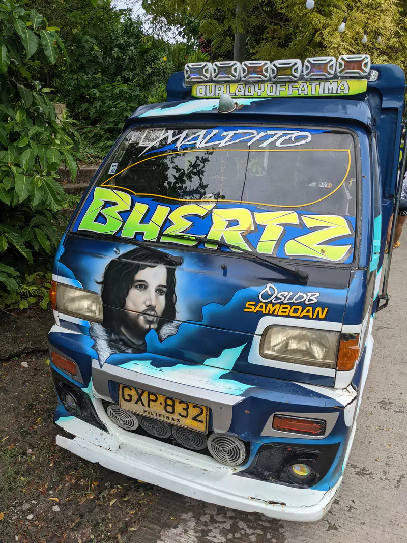 Colorful jeepney decorated with artwork including a portrait of Jesus, with the words 'Our Lady of Fatima' and 'Oslob Samboan' painted on the front.