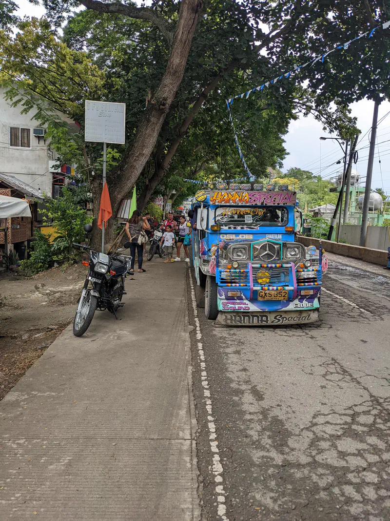 Colorful jeepney labeled 'Hanna Special' parked on the side of a street with people walking nearby under trees.