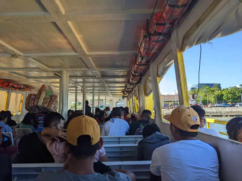 Passengers sitting on benches inside a ferry boat as it departs from the port.