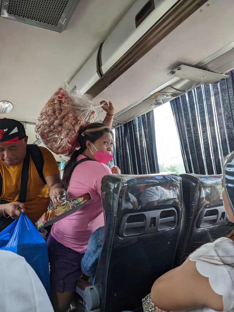 Woman with a large bag of snacks on her head selling inside a bus.
