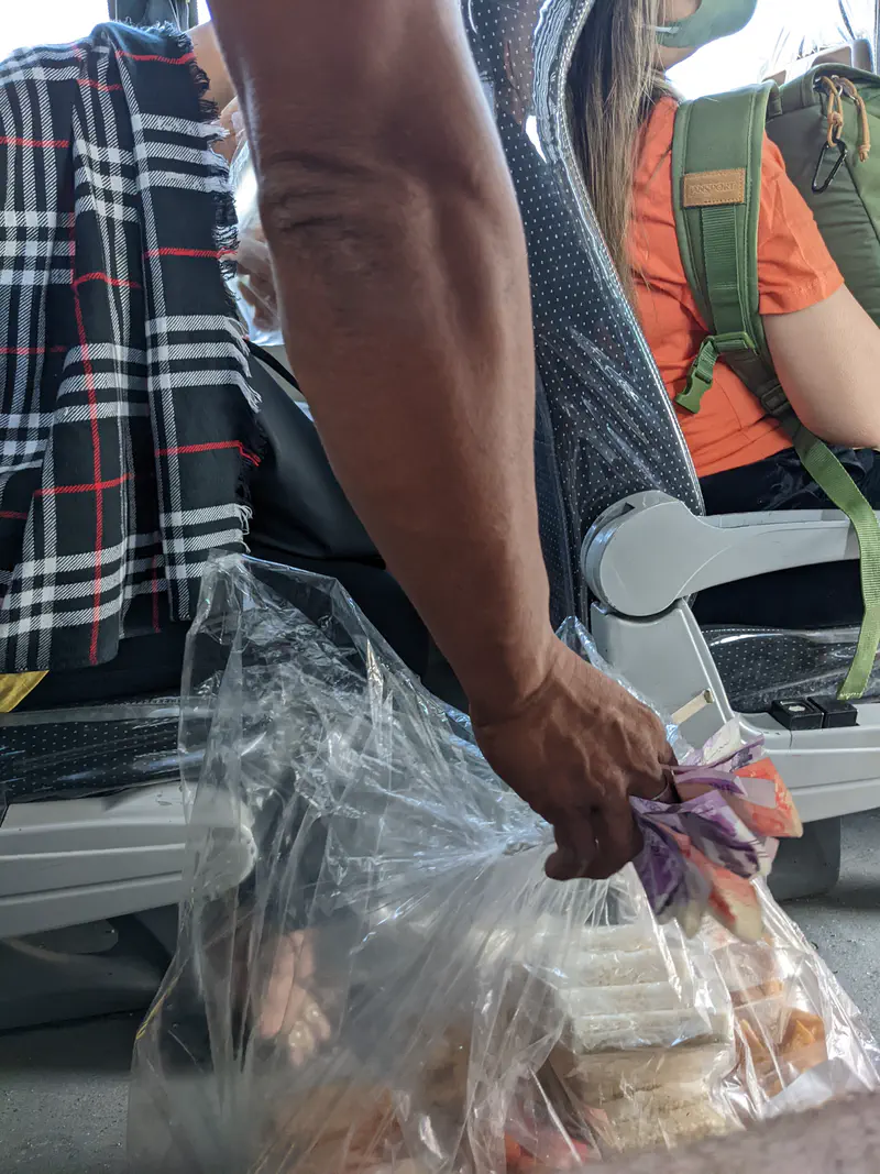 Close-up of a vendor’s hand holding money while selling food from a plastic bag on a bus.