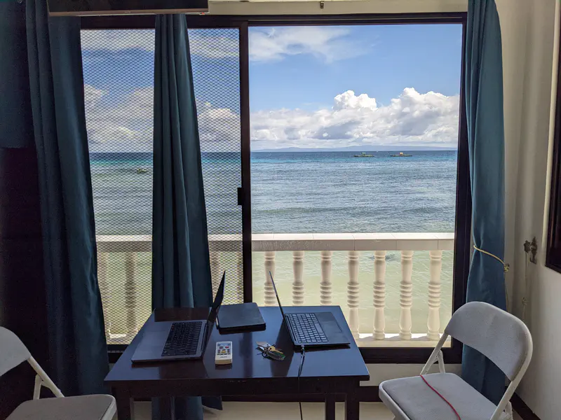 Small desk with two laptops facing a balcony overlooking the sea.