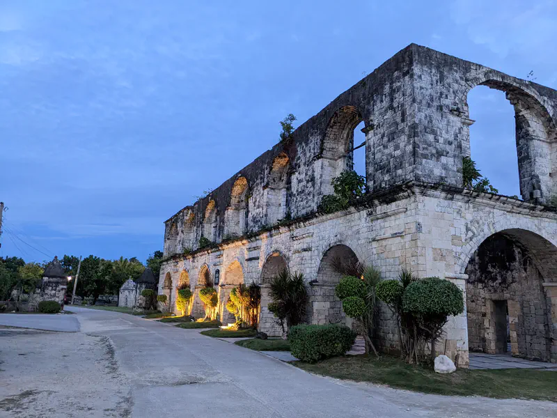 Old stone ruins with arched doorways and windows illuminated by lights at dusk.